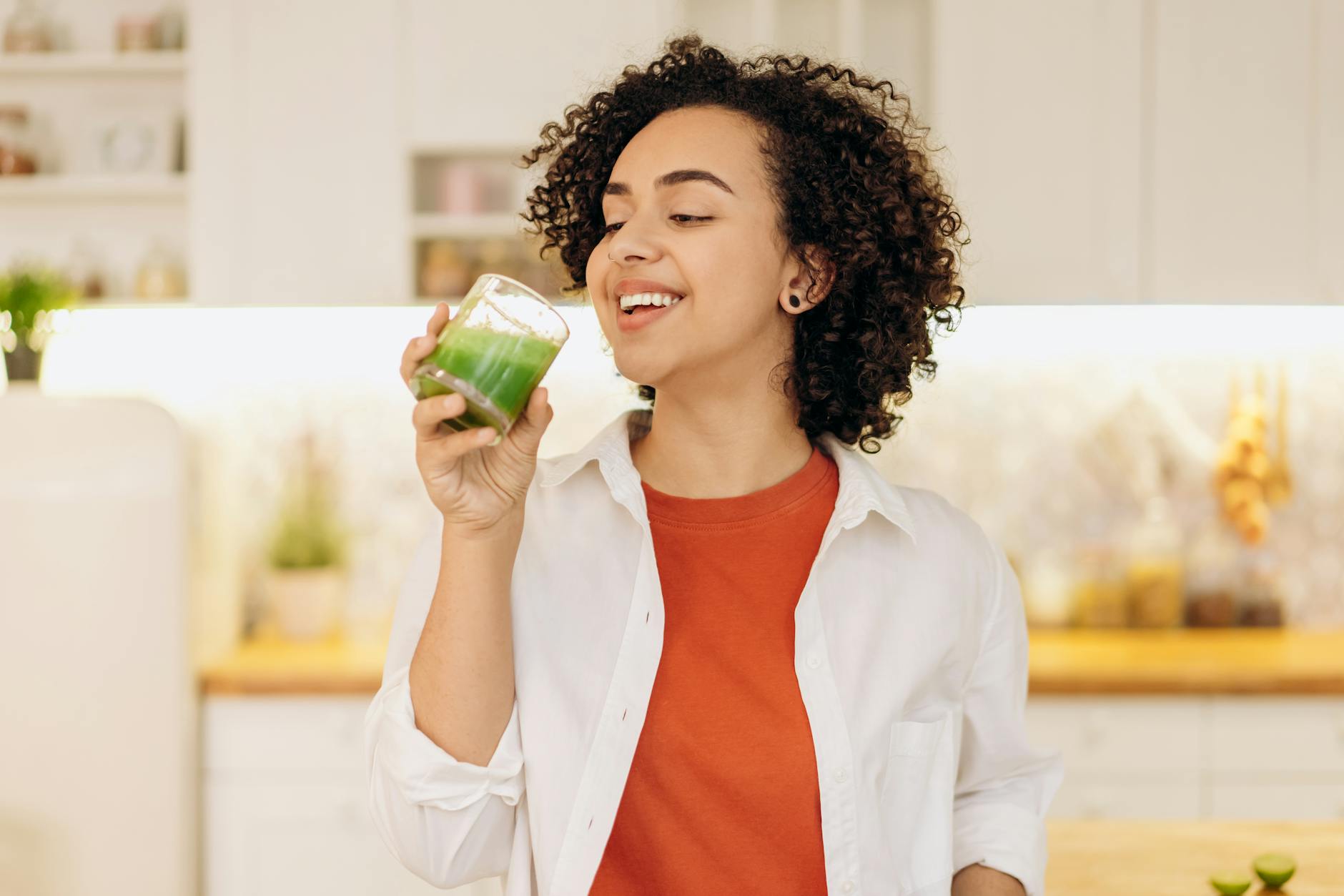 Smiling woman enjoys a fresh green smoothie in a cozy kitchen, promoting a healthy lifestyle. - spring detox cleanse
