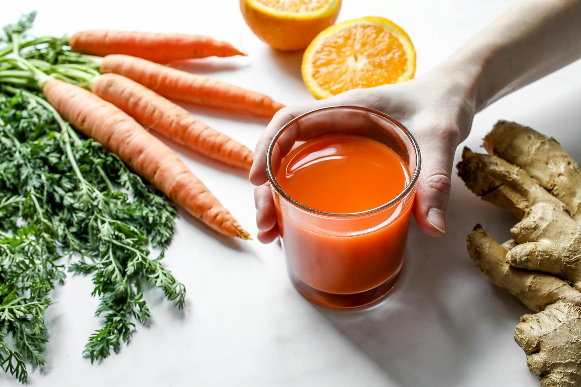 Vibrant carrot and ginger juice surrounded by fresh ingredients on a clean surface. - spring detox plan