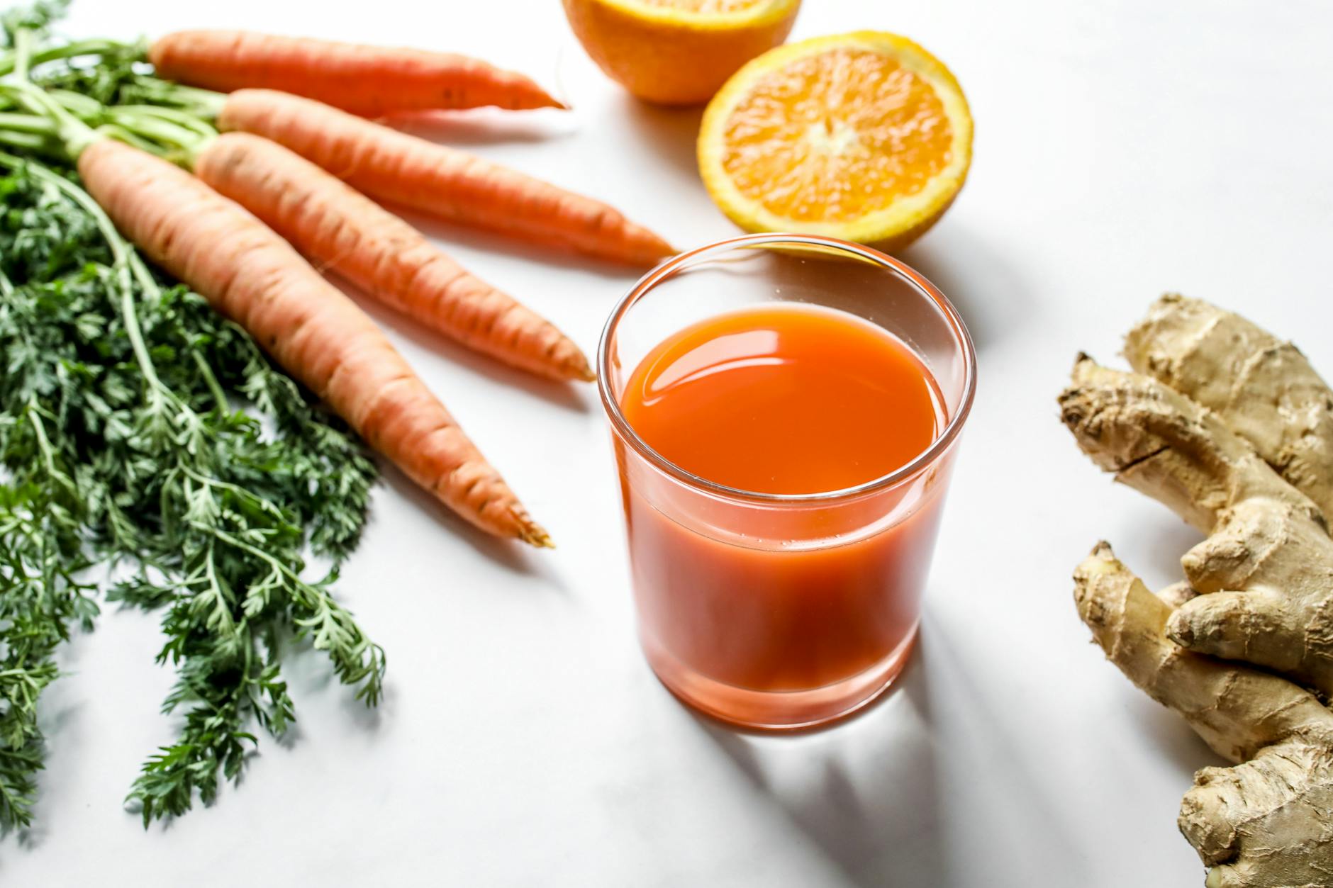 Fresh carrot ginger and orange juice surrounded by ingredients on a white background. - spring detox plan