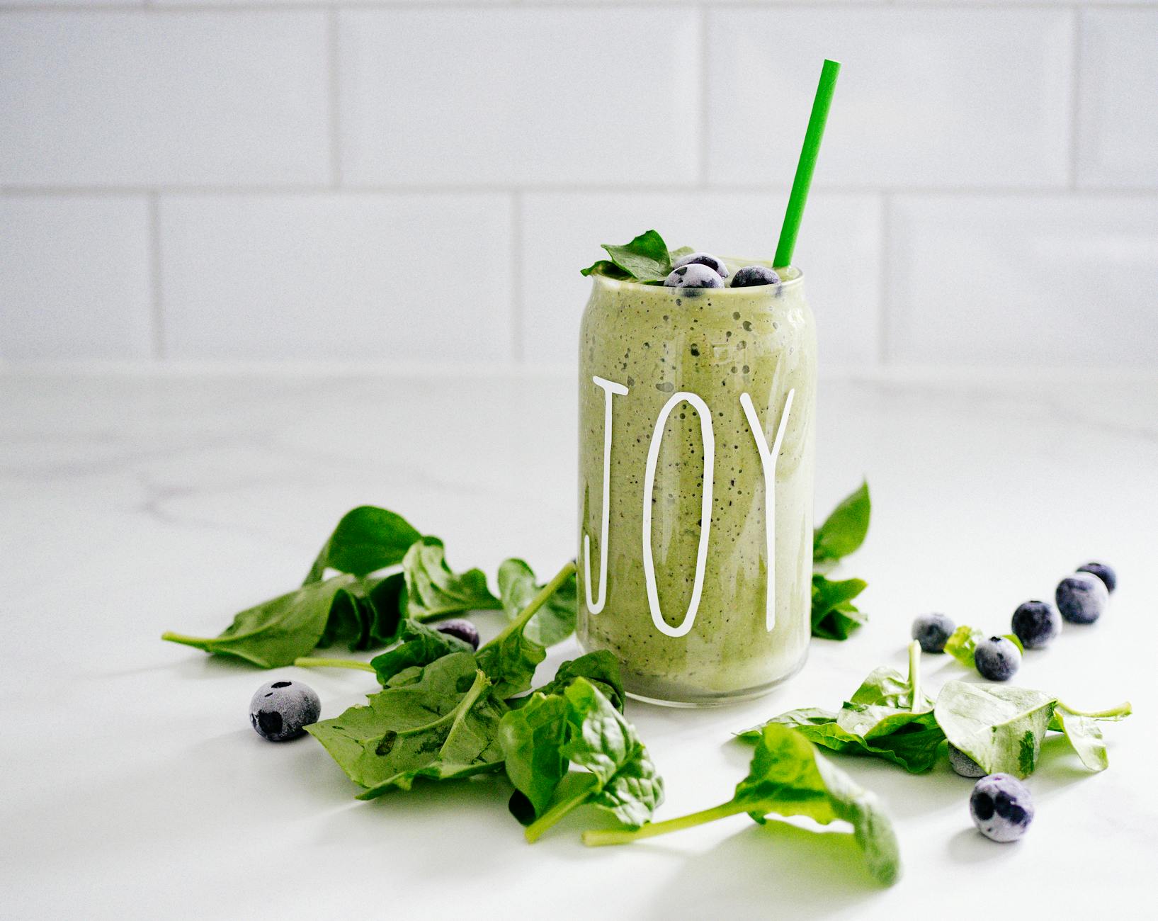 Refreshing green smoothie with spinach and blueberries in a glass labeled 'JOY' on a white background. - spring detox smoothie