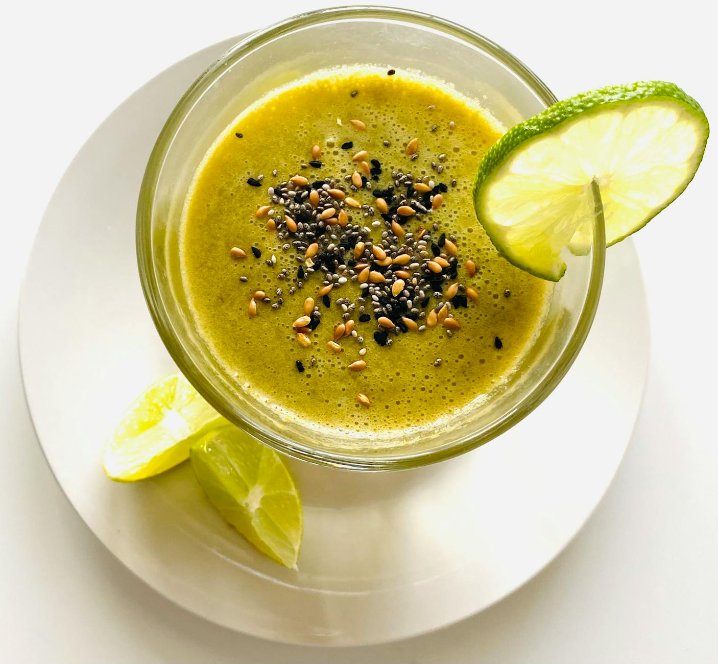 Overhead view of a green smoothie with sesame seeds and lime on a saucer. - spring detox smoothie