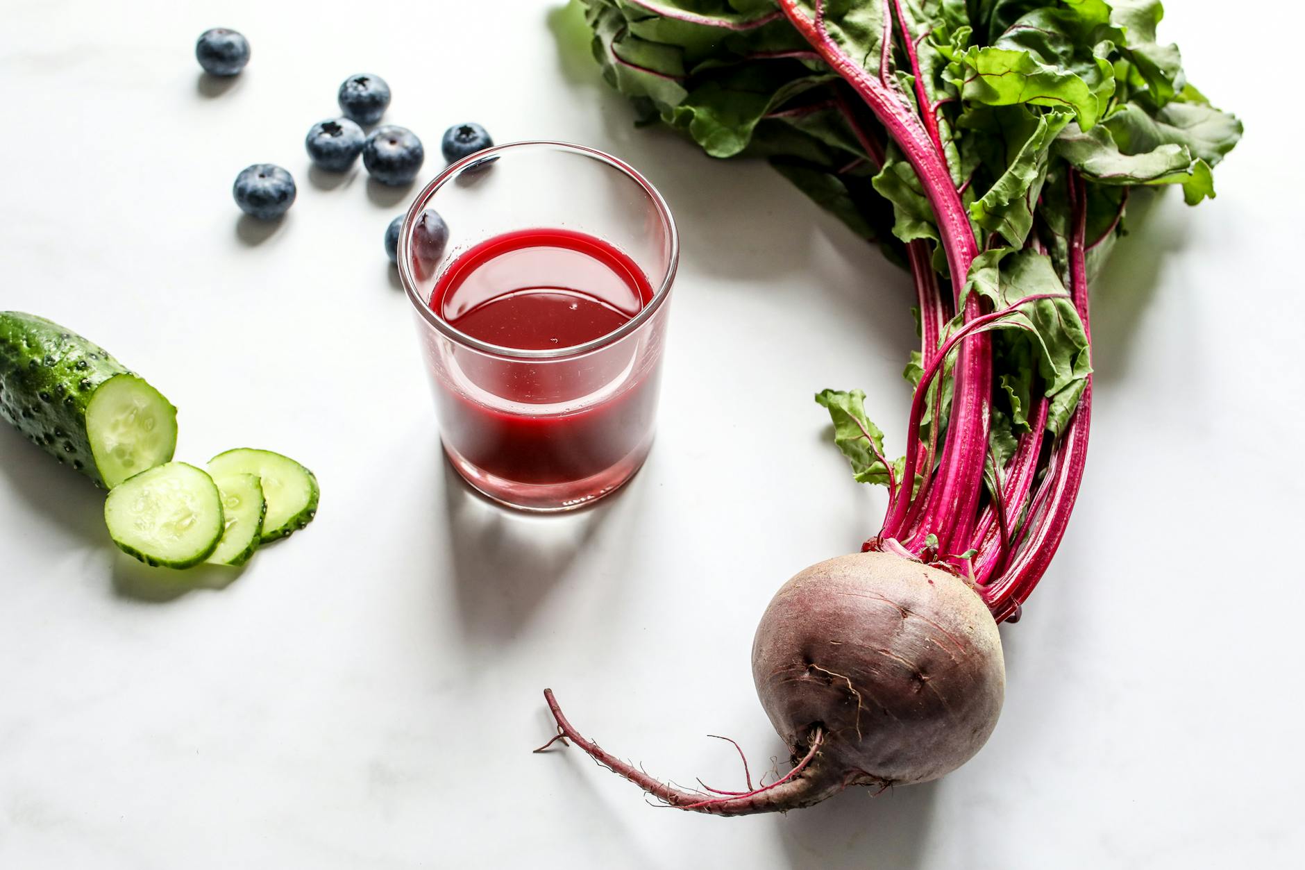 Nutrient-rich beetroot, cucumber, and blueberry juice with fresh produce on white background. - spring detox tips