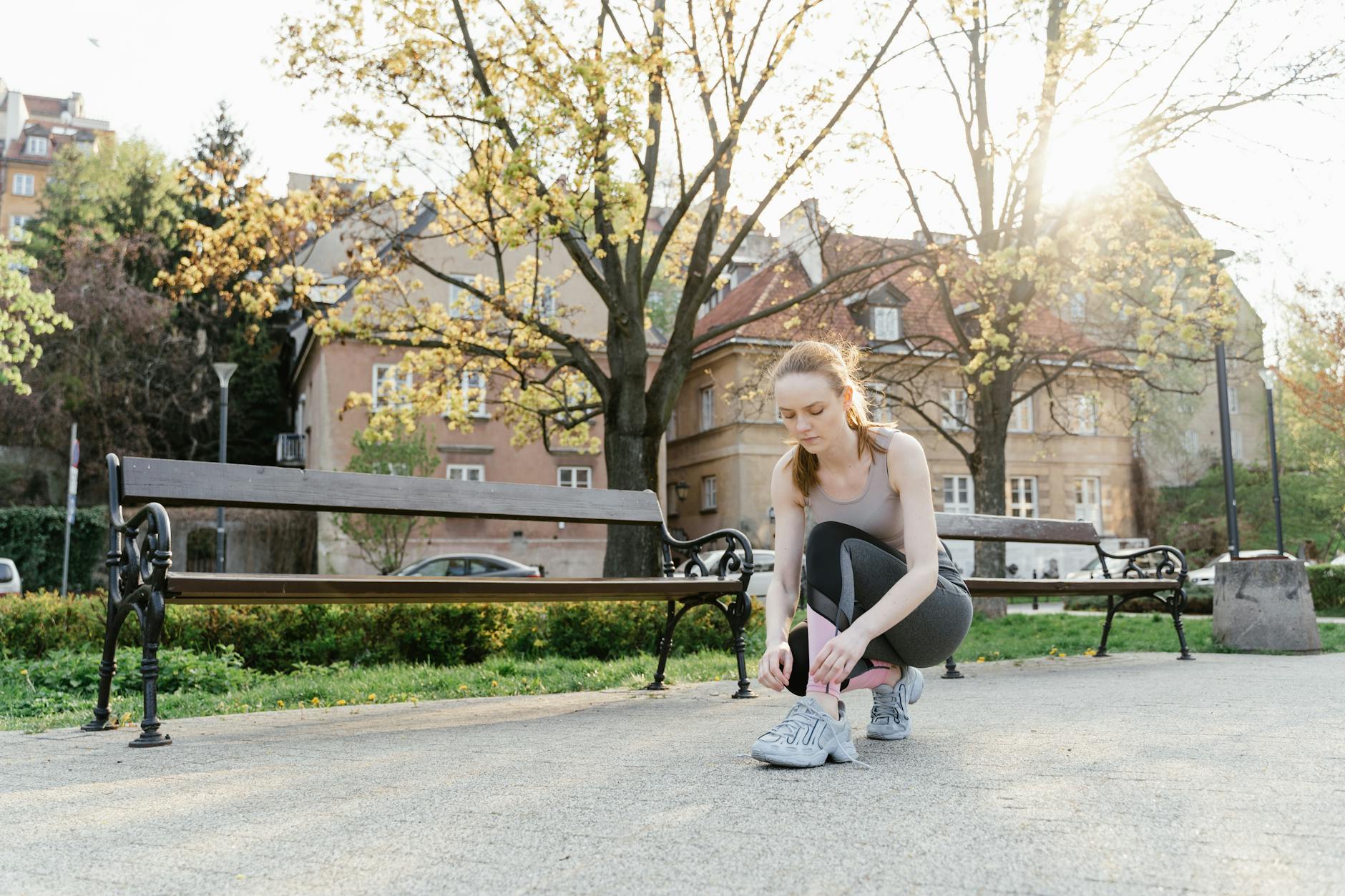 Woman tying shoelaces on a sunny day in a park, preparing for a workout. - spring exercise daylight
