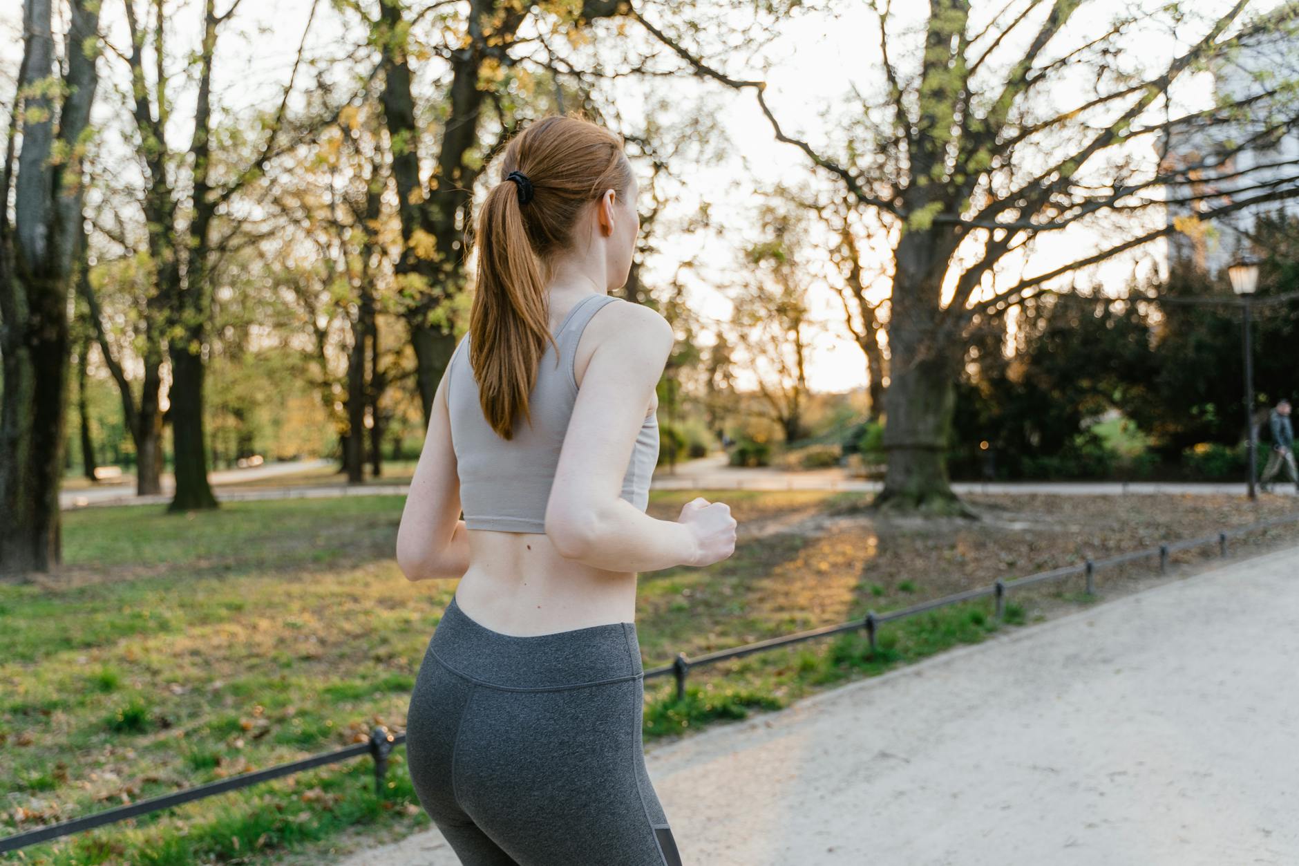 A woman jogs in a park during sunset, enjoying an outdoor fitness routine. - spring exercise motivation