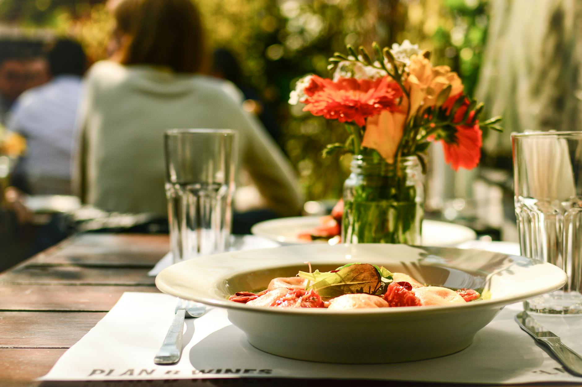 Delight in a cozy outdoor dining scene featuring a beautifully plated pasta dish and floral arrangements. - spring garden meals