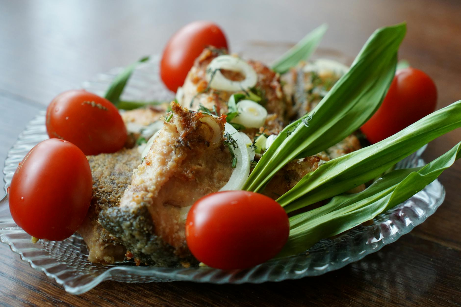 Mouth-watering fried fish served with tomatoes, onions, and green leaves on a glass plate. - spring garden meals