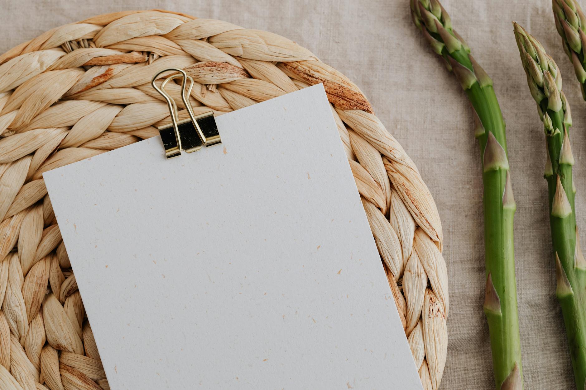 Top view of fresh asparagus next to a blank paper with a clip on rustic woven mat. - spring healthy recipes