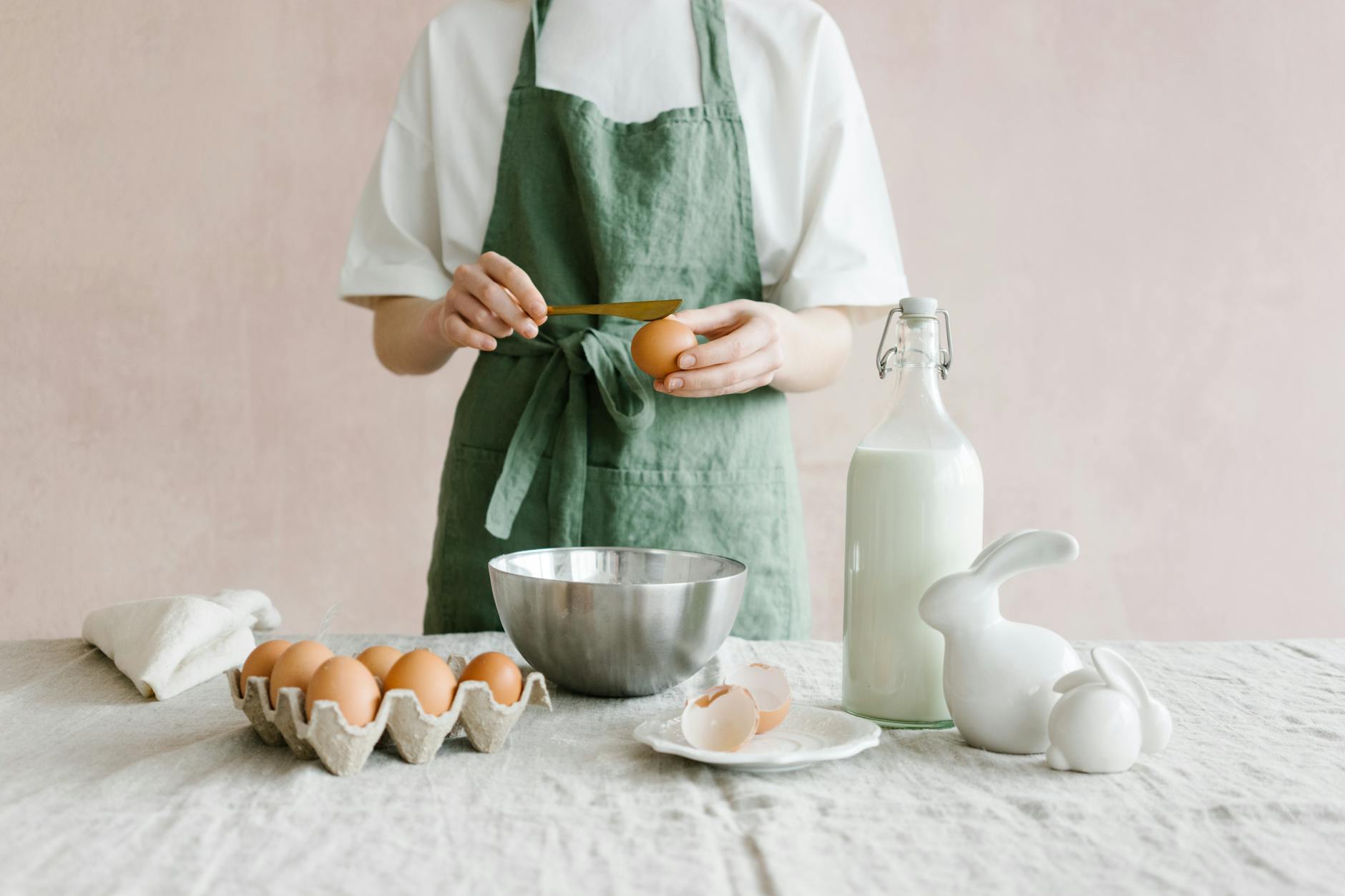 Crop anonymous female with egg in hand at table with iron bowl and glass bottle of milk - spring healthy recipes