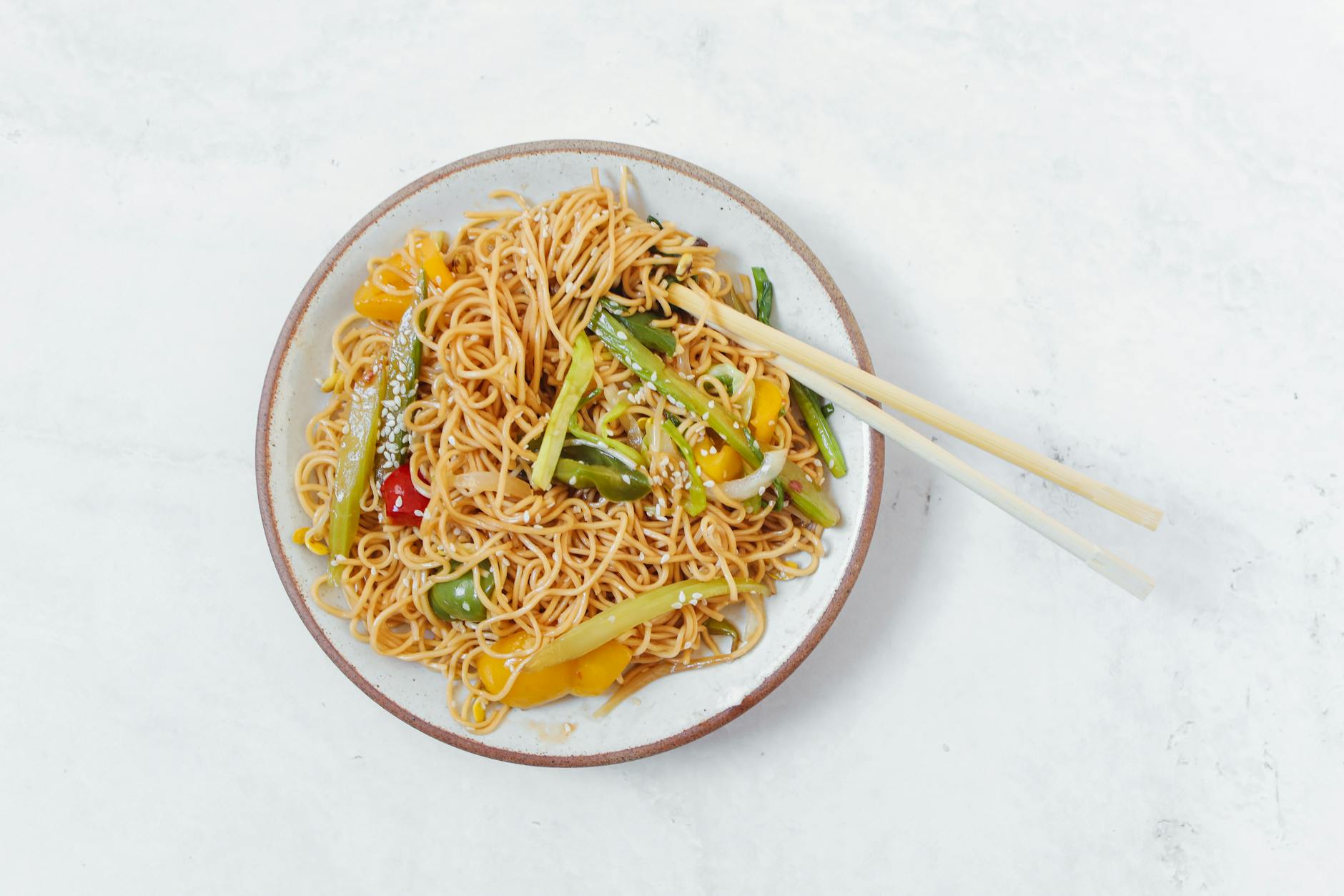 Appetizing plate of stir-fried noodles with colorful vegetables and chopsticks. - spring meal plan