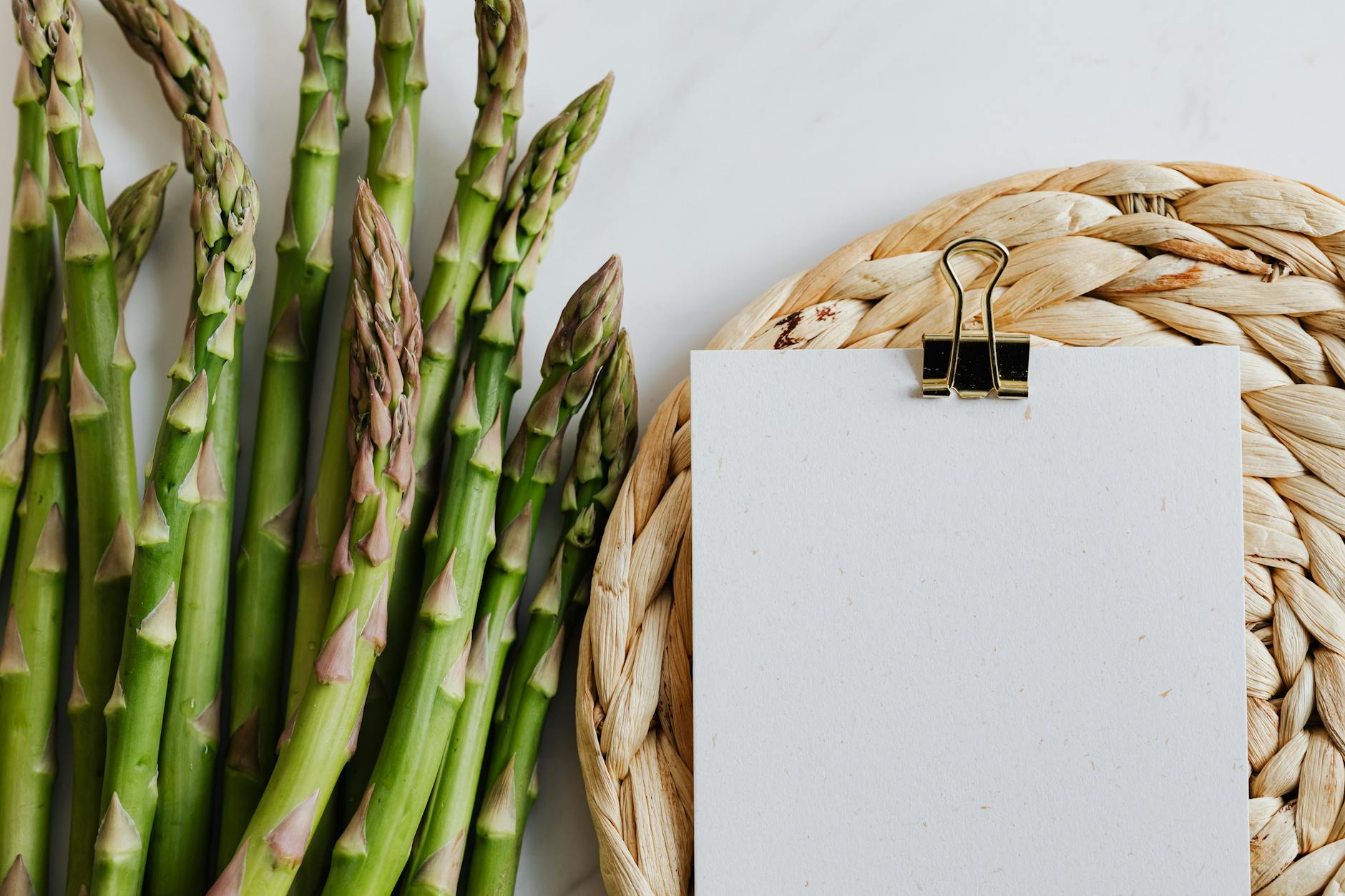 Top view of asparagus pods with sheets of paper fastened by paper clip on white desktop - spring meal plan