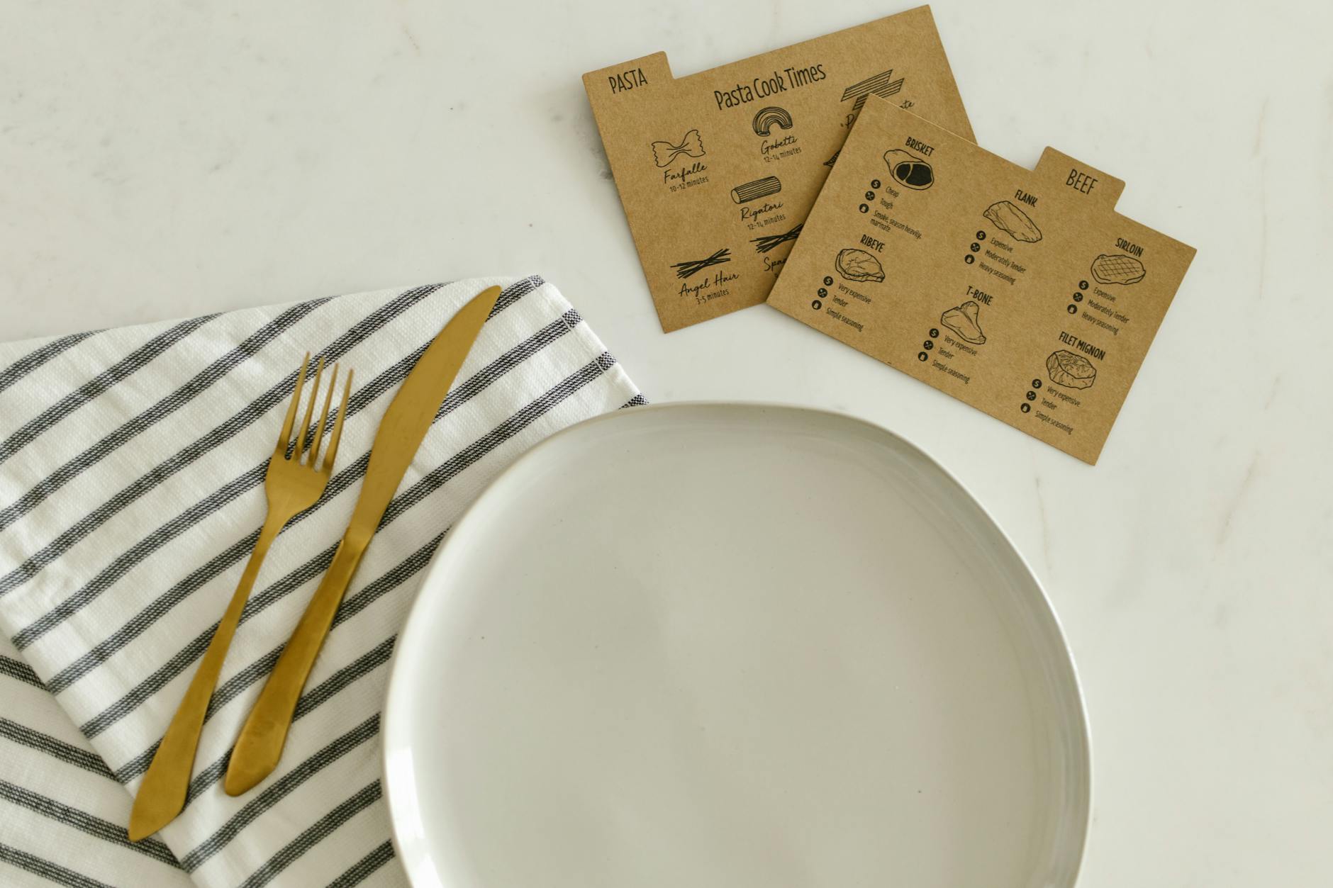 Top view of a ceramic plate with gold cutlery, striped napkin, and recipe cards on a marble table. - spring meal plan