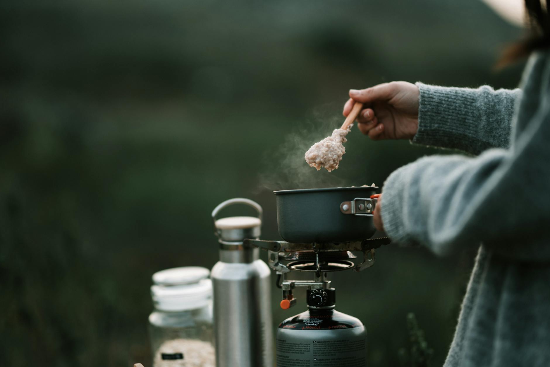 A person is cooking steaming oatmeal on a portable stove during a camping trip. - spring nutrition outdoor