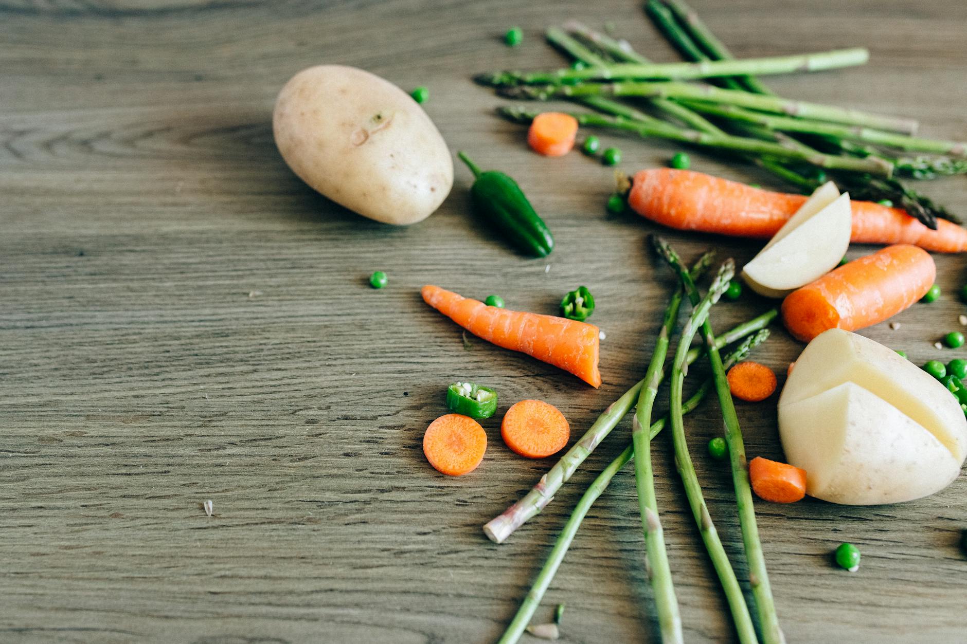 A variety of fresh organic vegetables including carrots, peas, and asparagus on a wooden surface. - spring produce nutrition