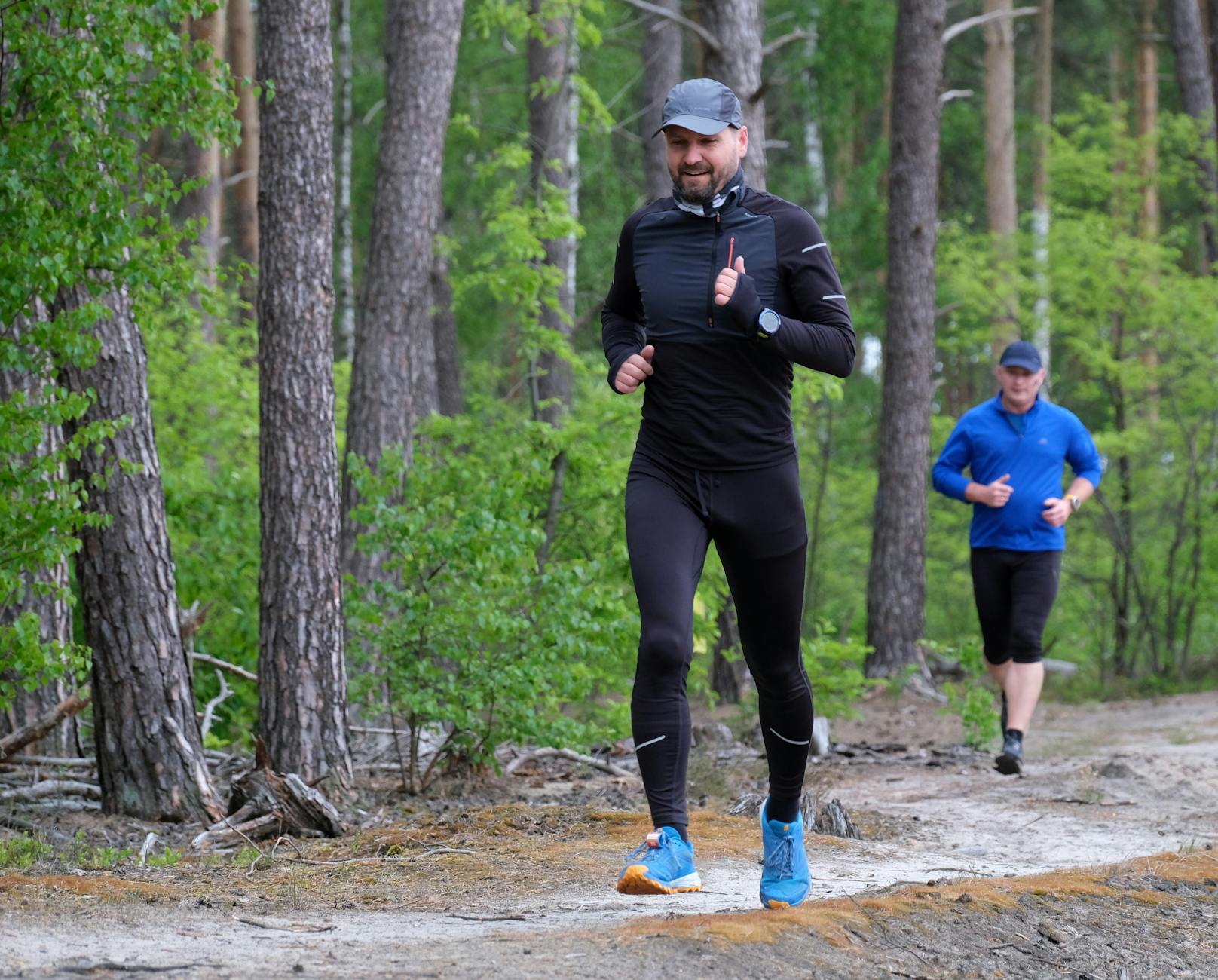 Outdoor exercise scene with two men jogging through a lush green forest trail, wearing sports attire. - spring run nutrition