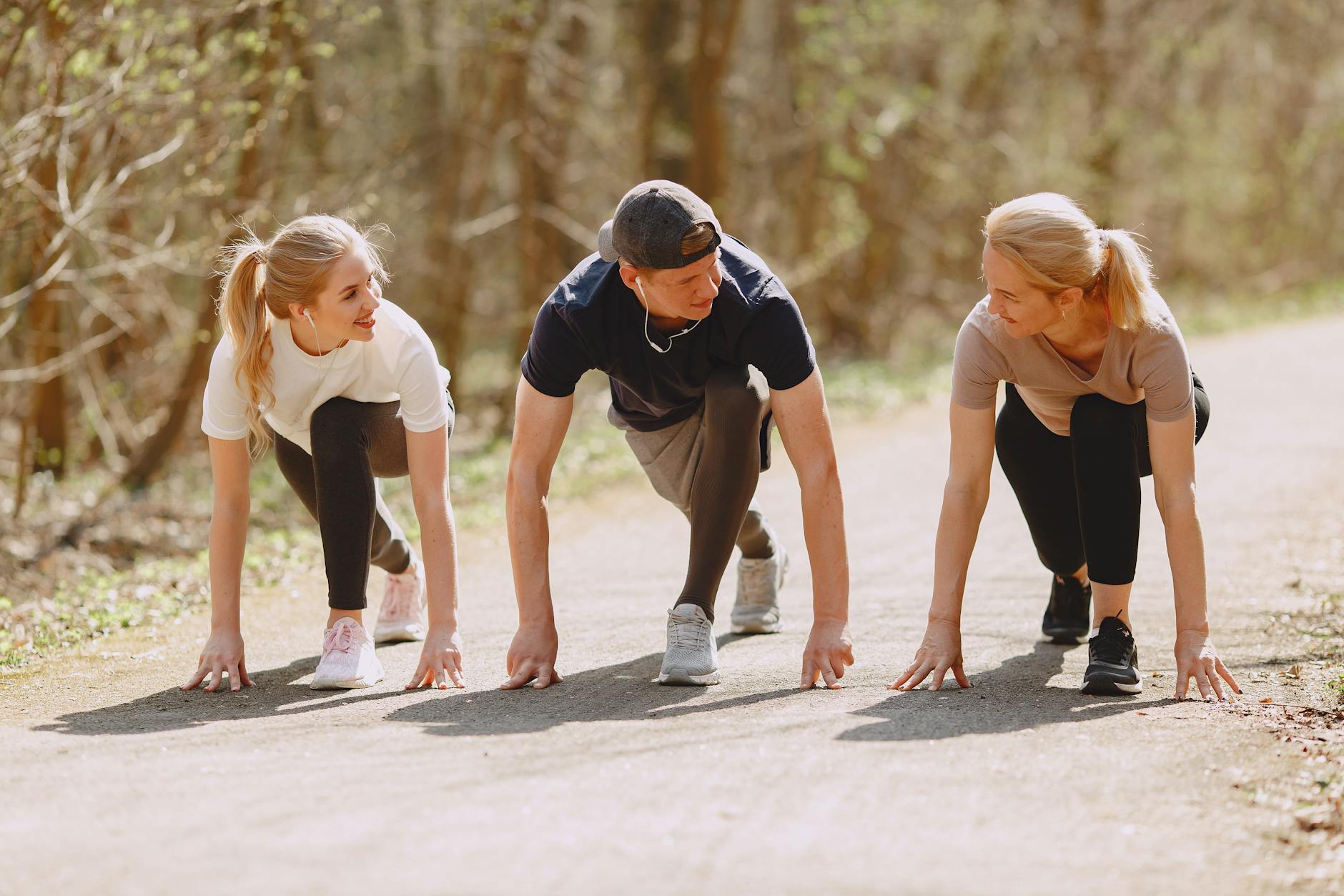 Group of cheerful athletes in sportswear in ready pose for sprinting together during fitness workout and running in spring park - spring running trails