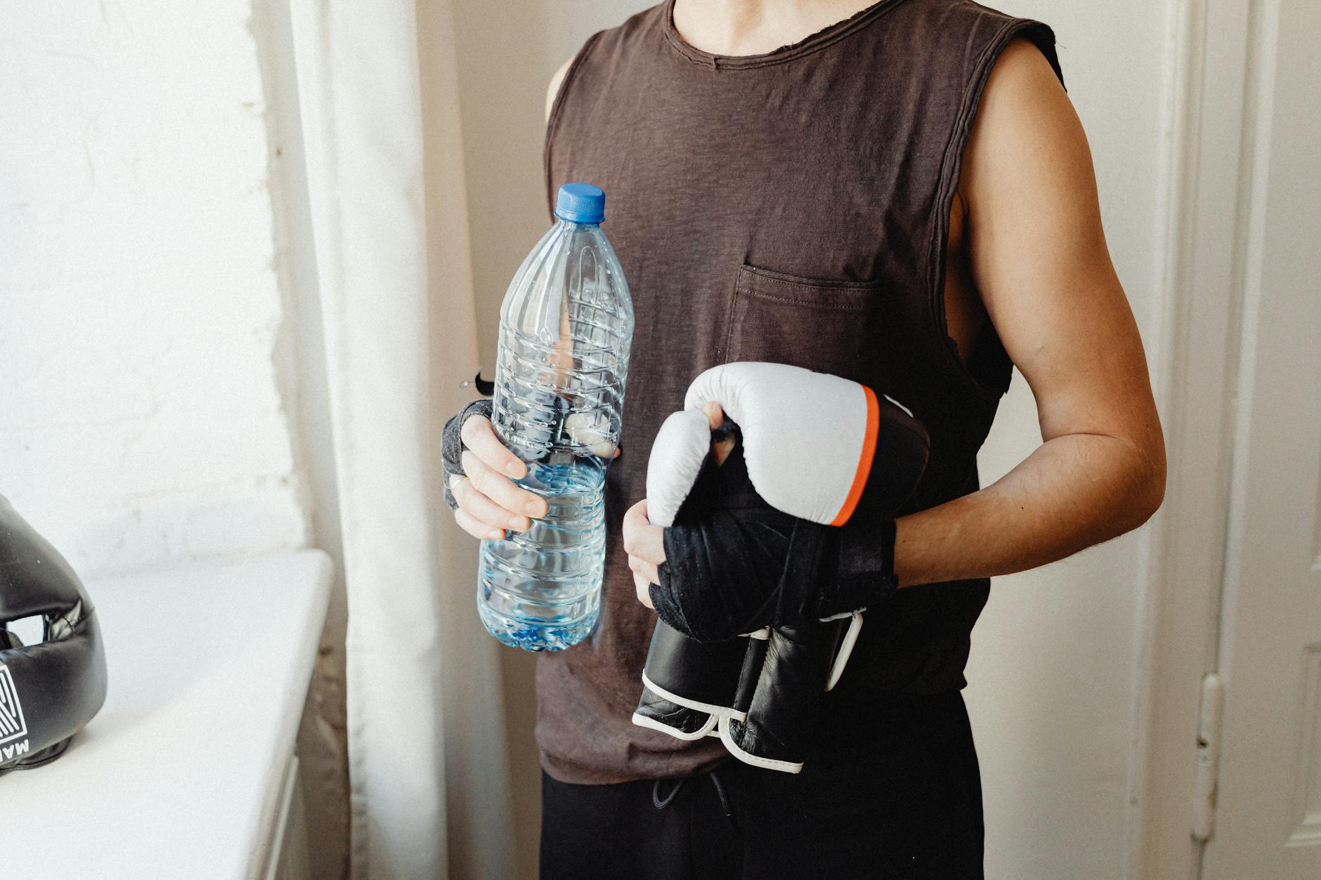 A male boxer holding a water bottle and boxing gloves, representing a healthy lifestyle. - spring sports hydration