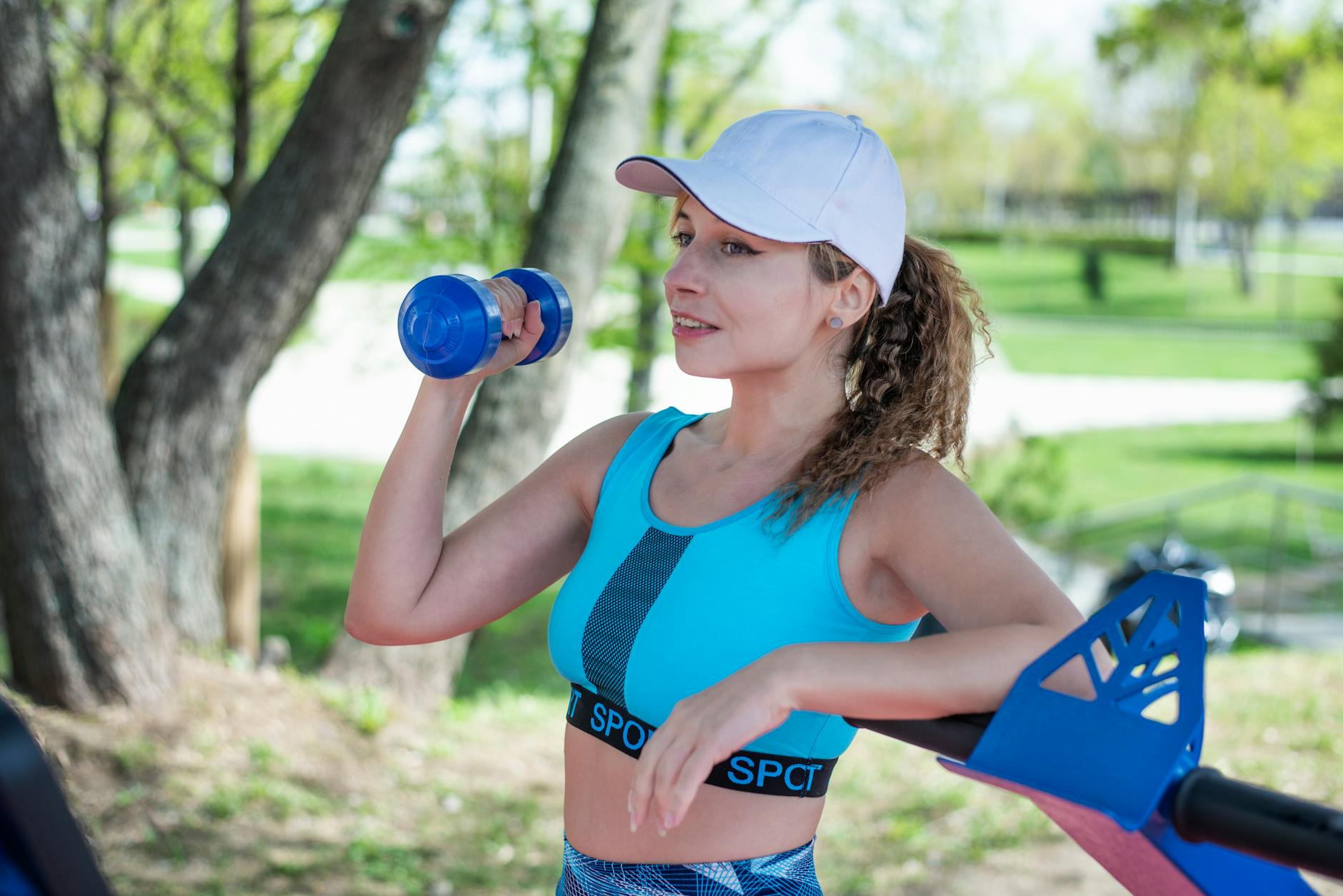 A woman in sportswear exercising with a dumbbell in a sunny park setting. - spring strength moves
