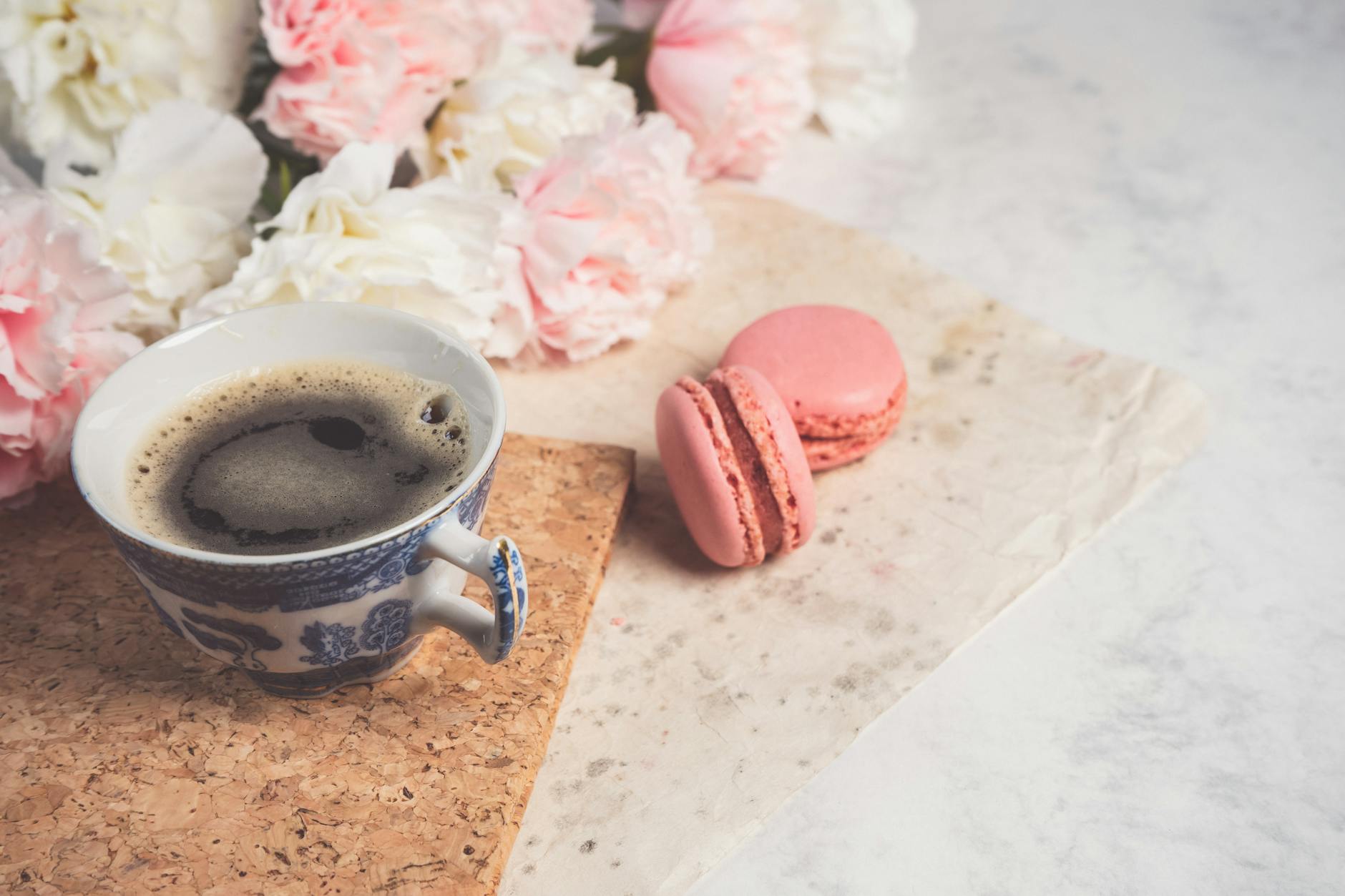A charming setup featuring a cup of coffee, pink macarons, and soft pastel flowers. - spring sweet cravings