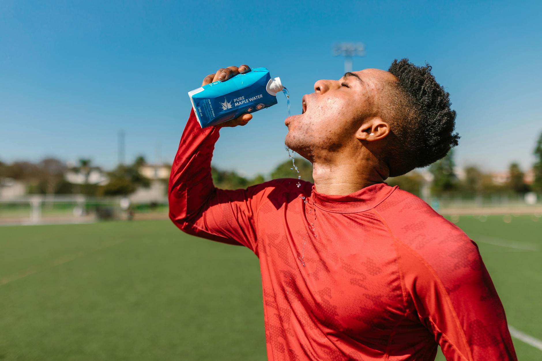 An athlete in a red shirt hydrates with maple water on a sunny day outdoors. - spring training hydration