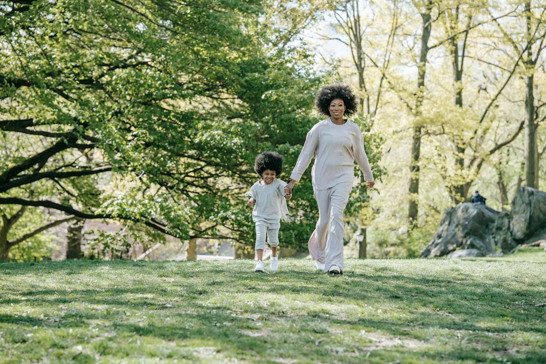 A mother and child holding hands, walking in a sunlit park surrounded by lush greenery. - spring wellness habits
