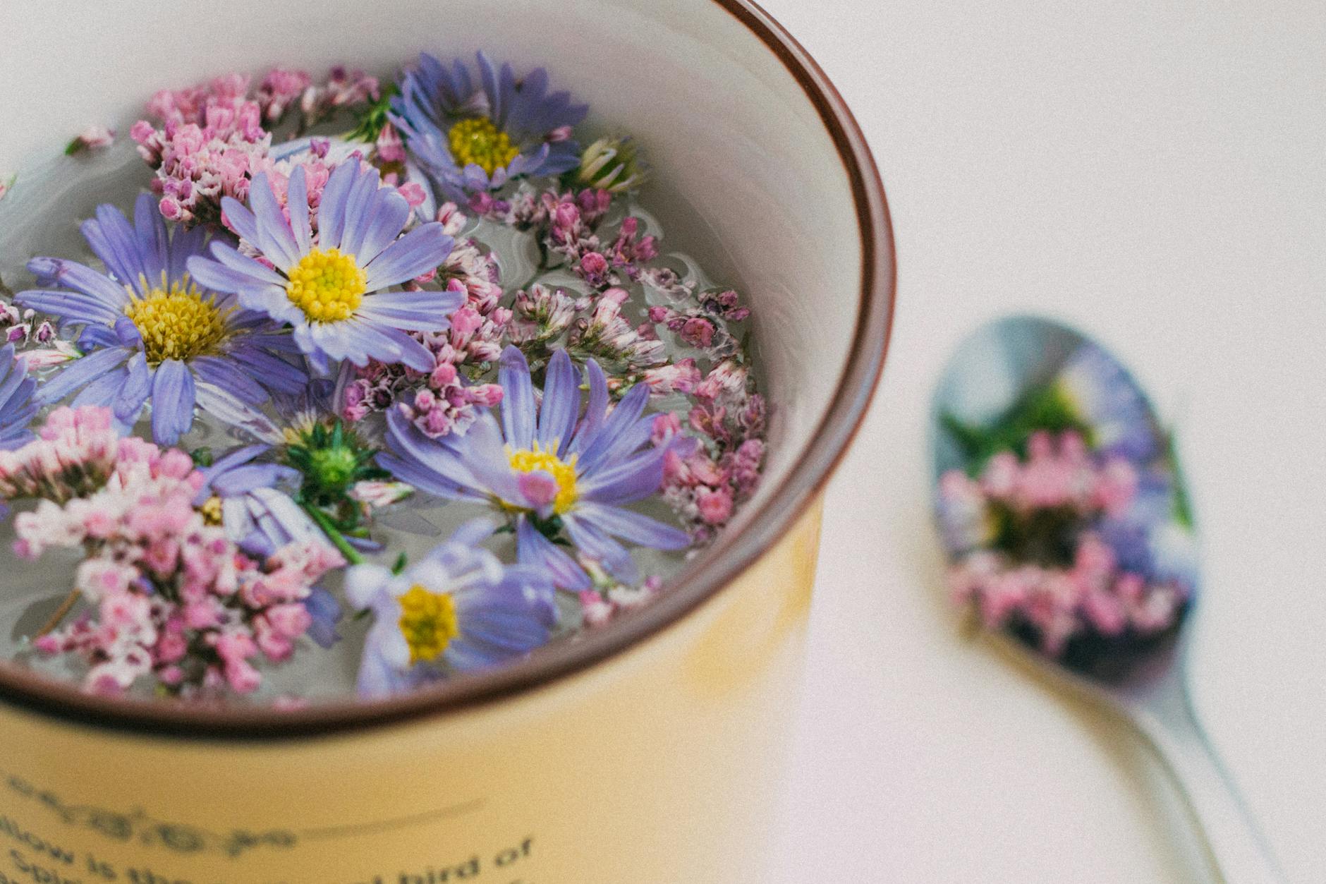 Delicate purple and pink flowers float in a cup, with a spoon reflecting floral patterns. - spring wellness habits
