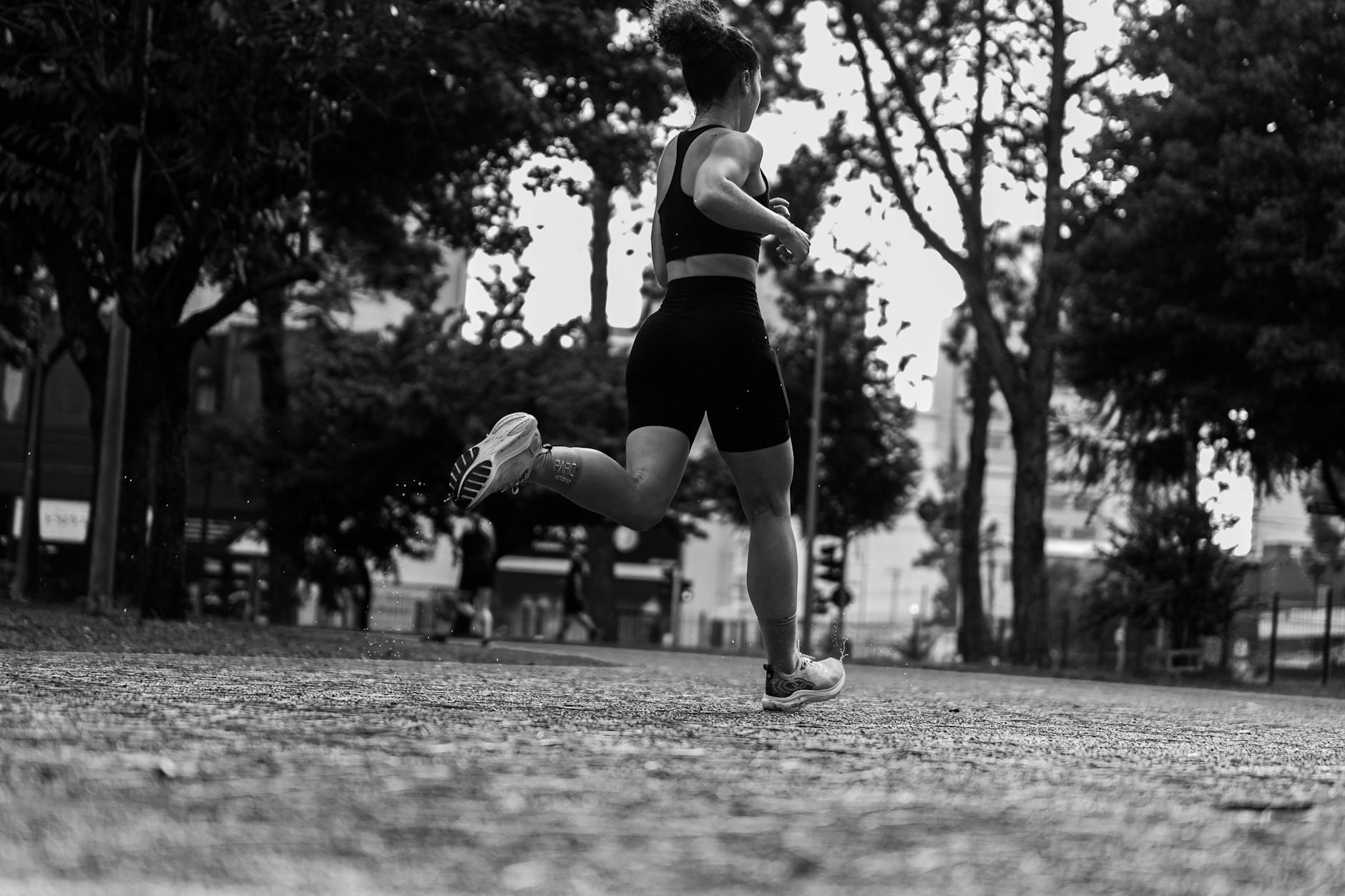 Dramatic black and white photo of a woman running through a park. - strength training runners