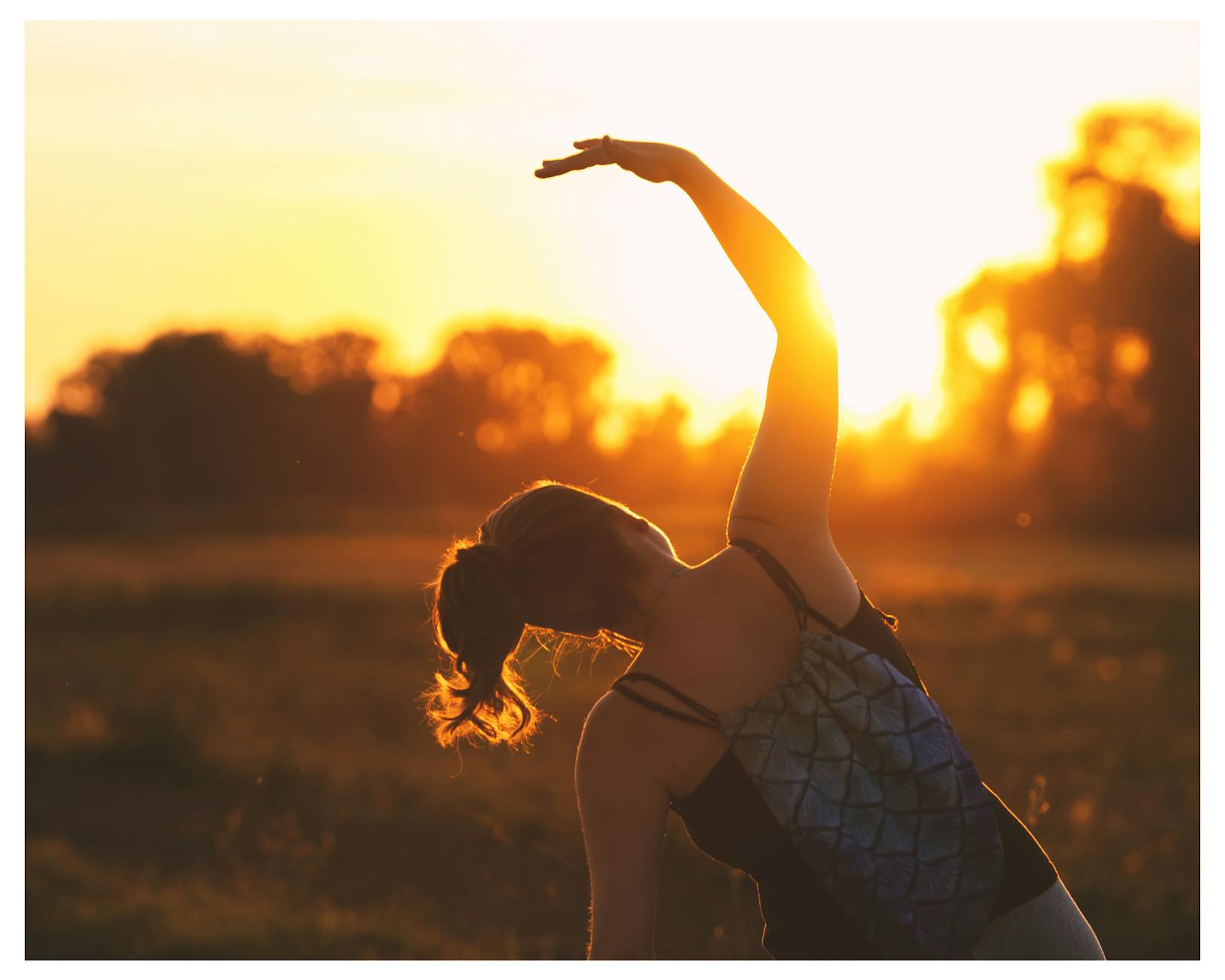A woman performs a stretching exercise outdoors at sunrise, embracing fitness during the serene golden hour. - sunrise yoga spring