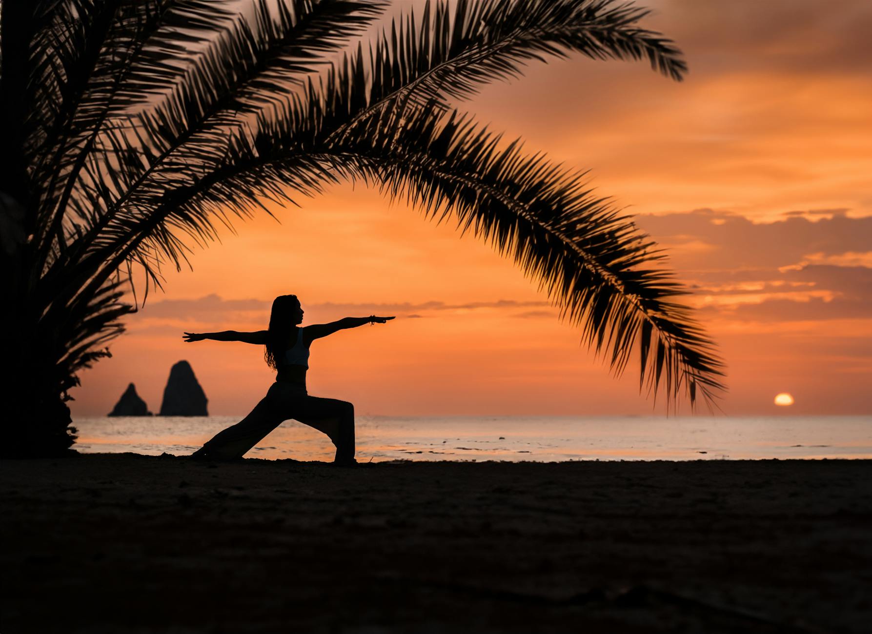 A woman practices yoga under palm trees during a vibrant sunset on a tropical beach. - sunrise yoga spring