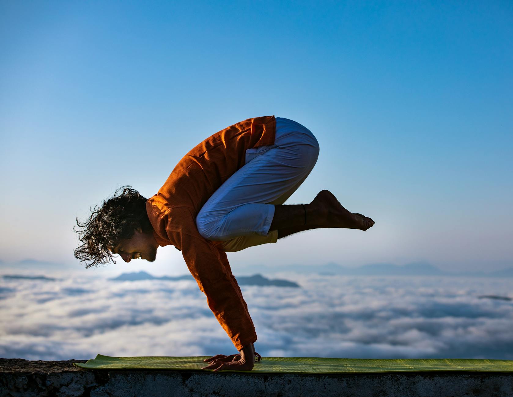 Person performing yoga on a mountain edge above the clouds. - sunrise yoga spring