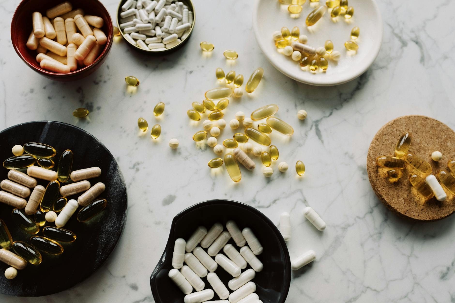 From above of various types of medication pills and yellow capsules of omega placed on different plates and stands on table - vitamin d mood