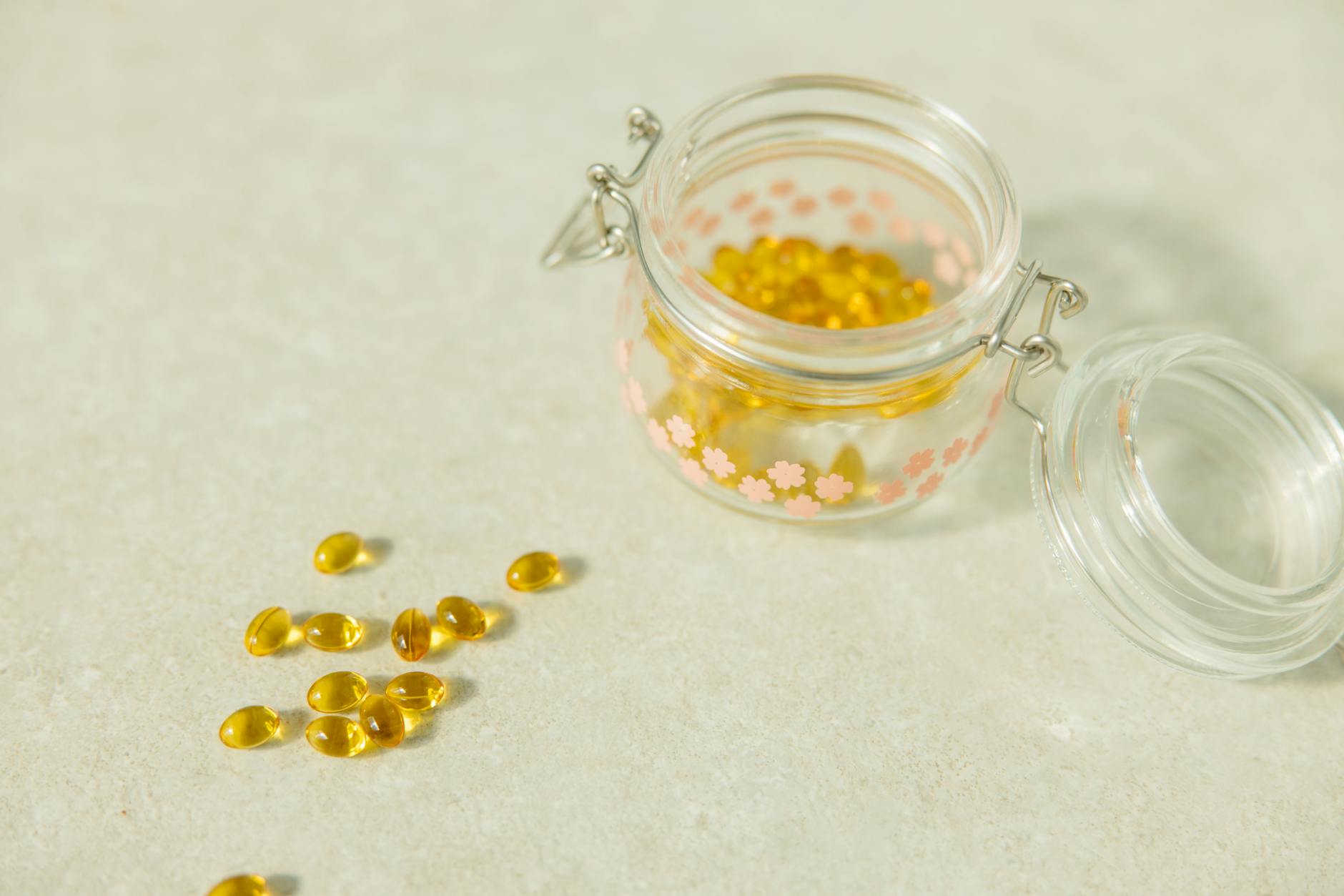 Close-up of open glass jar filled with yellow health capsules on light surface. - vitamin d mood