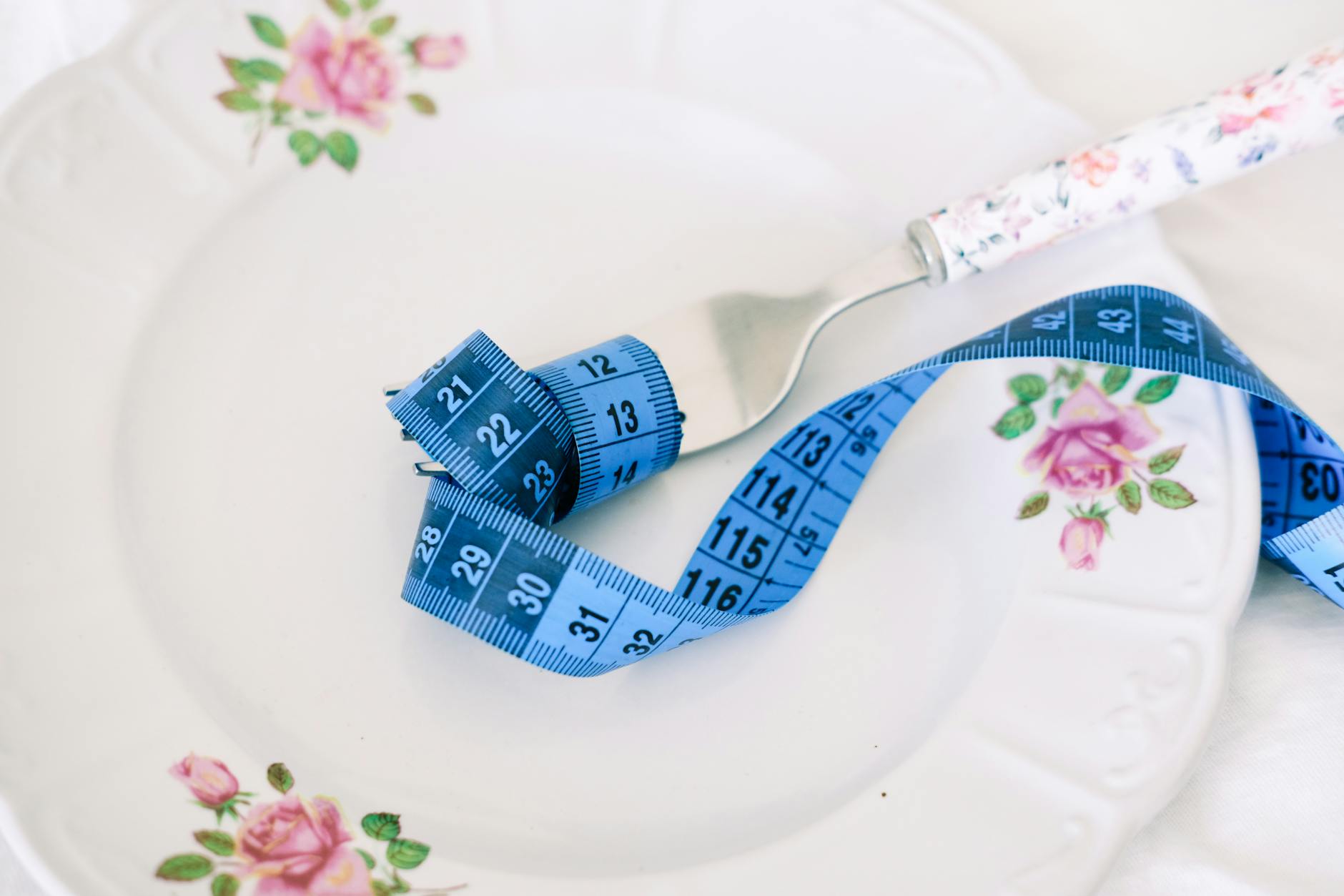 A floral plate with a fork and blue measuring tape symbolizing dieting or healthy eating. - weight loss jumpstart