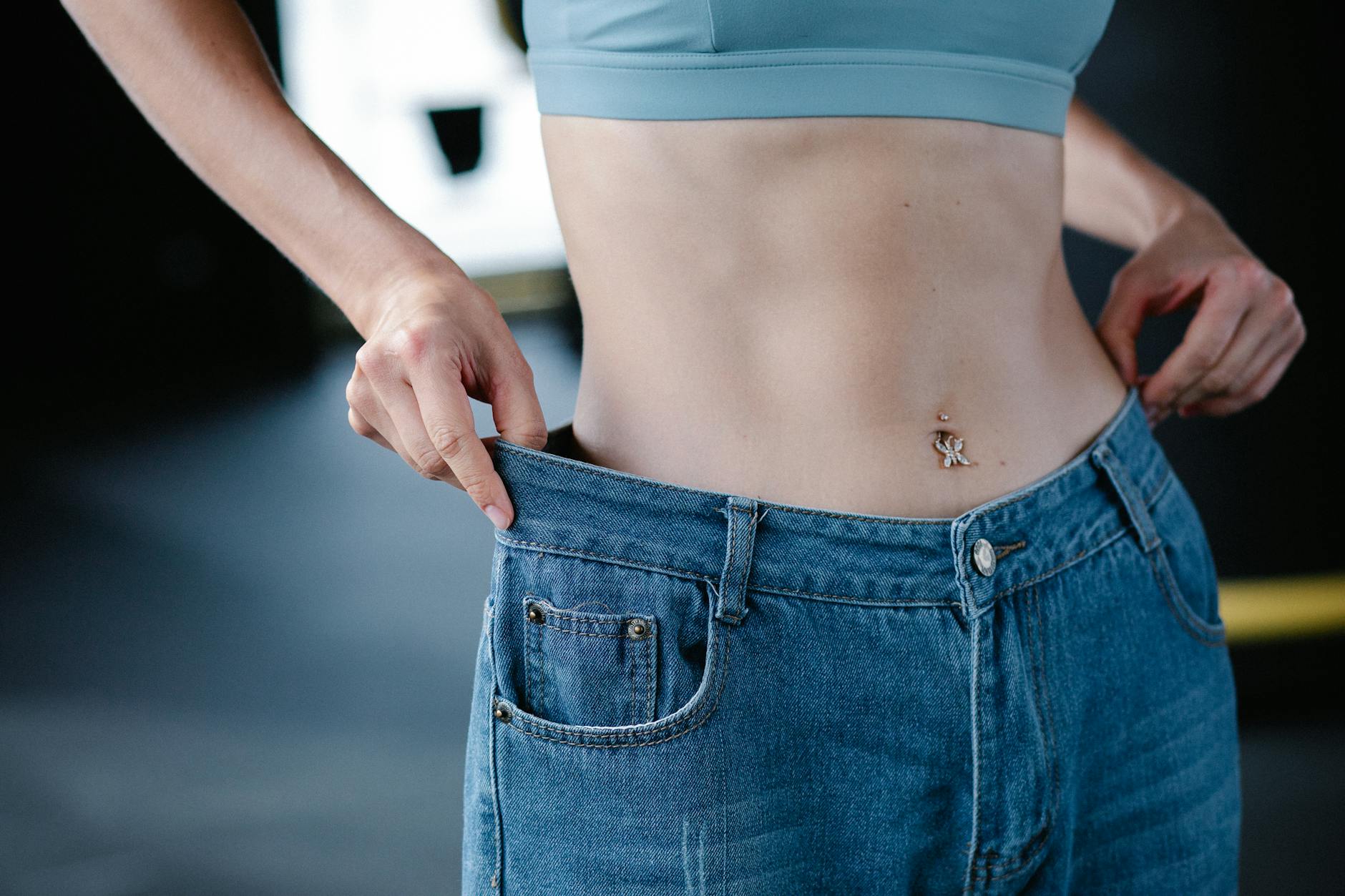 Close-up of woman pulling oversized jeans, illustrating weight loss. - weight loss jumpstart