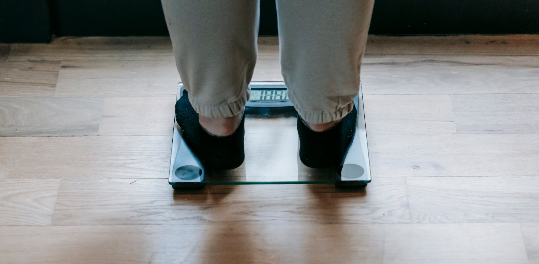 Back view of crop faceless obese female in socks weighing on glass scale placed on wooden floor in light room in daytime - weight loss jumpstart