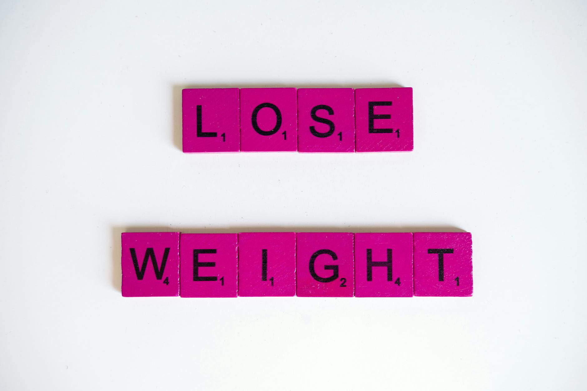 Creative image of the phrase 'Lose Weight' spelled with Scrabble tiles on a white background. - weight loss motivation